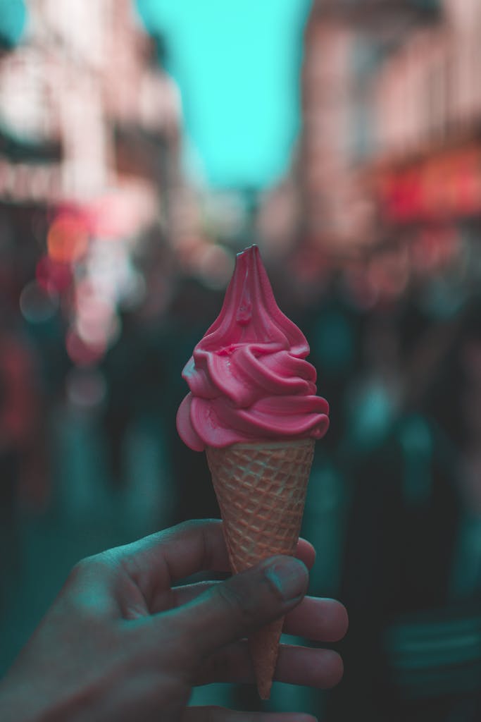 A hand-held pink ice cream cone on a bustling Paris street.