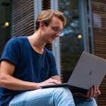 A young man sitting outdoors in Leiden, Netherlands, working on a laptop.