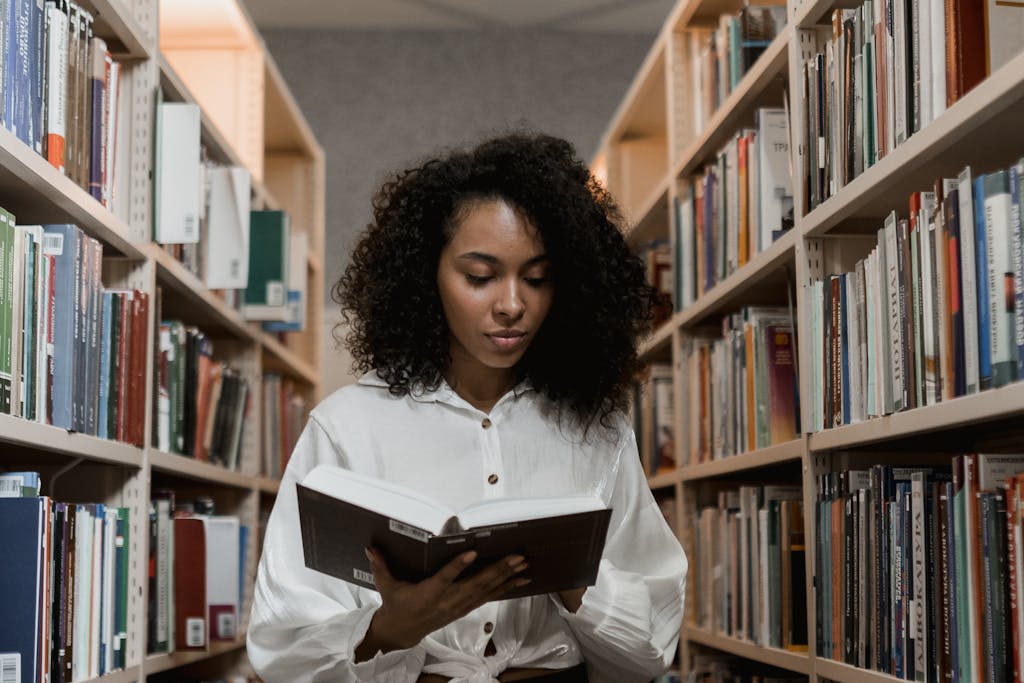 African American woman with curly hair standing in a library reading a book.