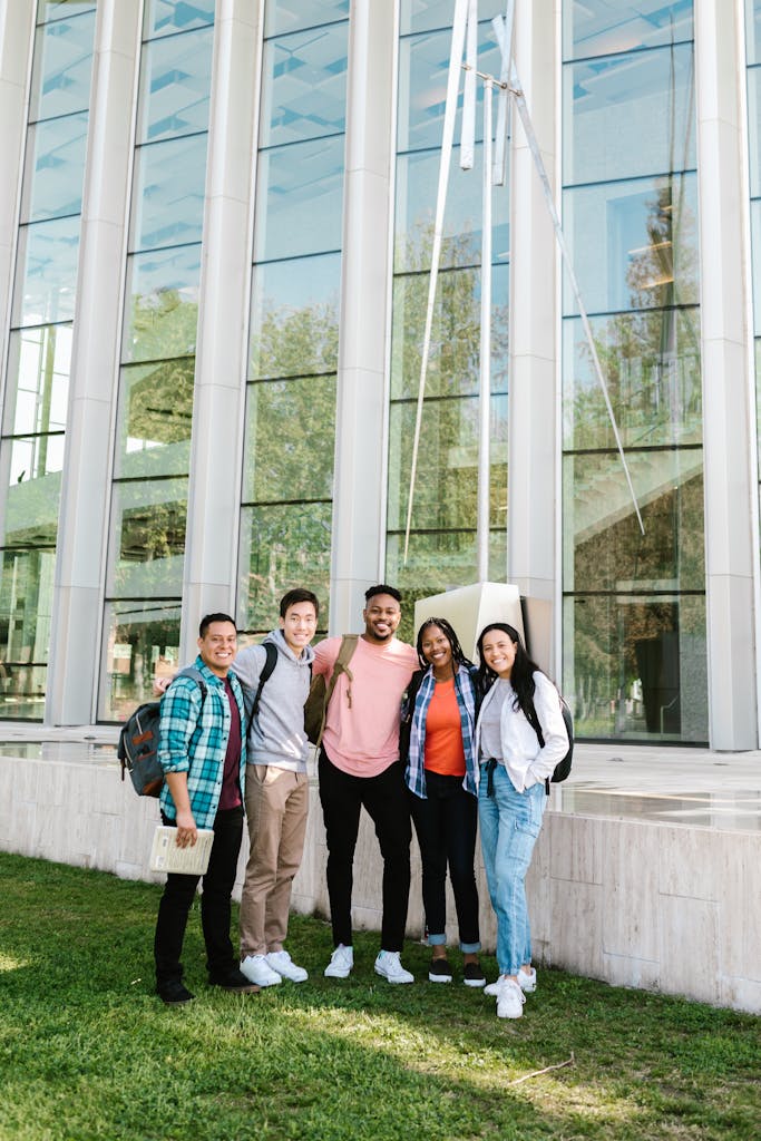 Cheerful group of diverse students standing outside a modern educational building on a sunny day.