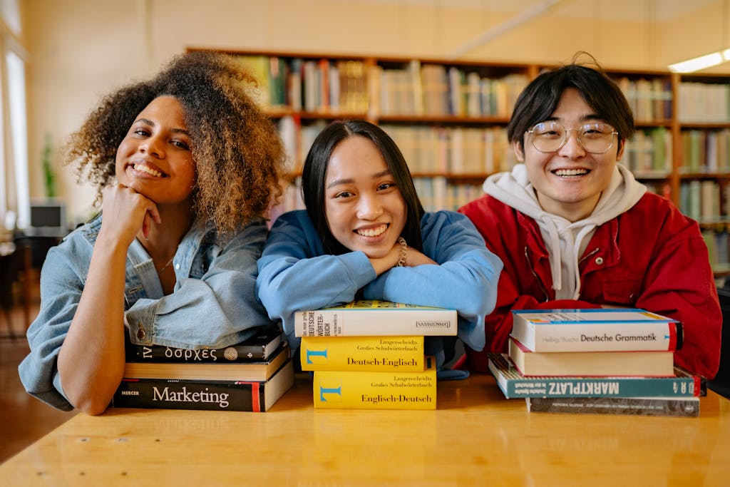 Three happy students in a library with language and marketing books.
