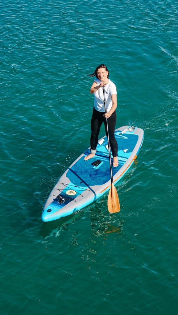 Woman enjoying a day paddleboarding on clear blue ocean water, captured from above.